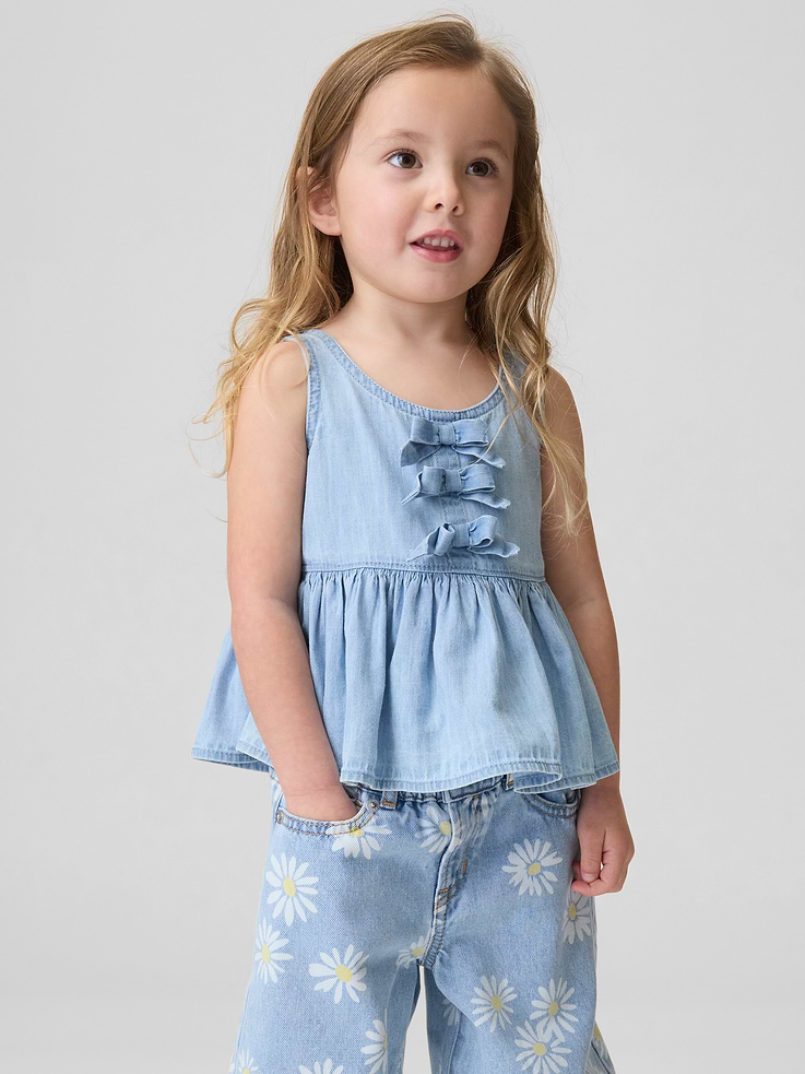 Image 1 of 3, Soft denim tank top., Round neck., Tank straps., Bow detail at front., Peplum hem., Responsibly Made: This top is part of our water-saving Washwell program. Compared with conventional wash methods, Washwell uses at least 20% less water., This product was made in a factory that invests in gender equity and women’s empowerment through RISE. Learn more at gapinc.com/equity ., Product #881738