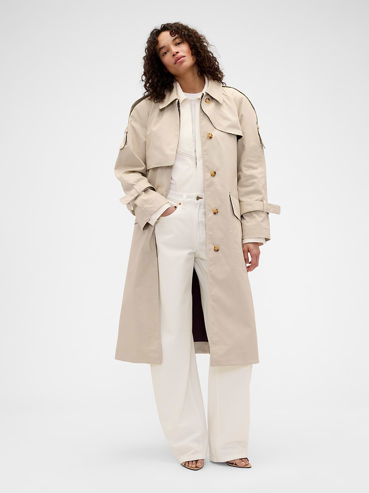 Image 1 of 4, Known for her timeless silhouettes and immaculate tailoring, Victoria Beckham's singular take on style is rooted in a sense of sophisticated ease. Through her lens, our icons take on a new form. Feminine. Powerful. Artistic. Grounded in elevated staples — and denim. The unexpected meeting of Victoria Beckham and Gap., Crisp, heavyweight cotton trench coat. In an oversized fit., Spread collar., Long sleeves with detailing at cuffs., Epaulettes on shoulder., Storm flaps at chest., Half-hidden belt at waist., Pockets at front., Slit at back hem., Inner contrast lining., This product was made in a factory that invests in gender equity and women’s empowerment through RISE. Learn more at gapinc.com/equity ., Product #903434