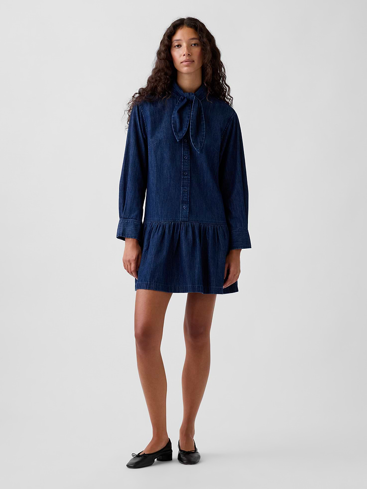 Image 1 of 5, Authentic, non-stretch denim shirtdress. In an ultra mini dress., Tie neck, button front., Long sleeves with button cuffs., Back yoke seam., Shirring at drop waist seam., Dark wash., This product is part of our water-saving Washwell program. Compared with conventional wash methods, Washwell uses at least 20% less water., Made with 55% Protocol cotton verified by the U.S. Cotton Trust Protocol, a program which works with farms committed to improving their environmental footprint by minimizing water usage and improving soil health (Claim No. 10127)., Product #1185335