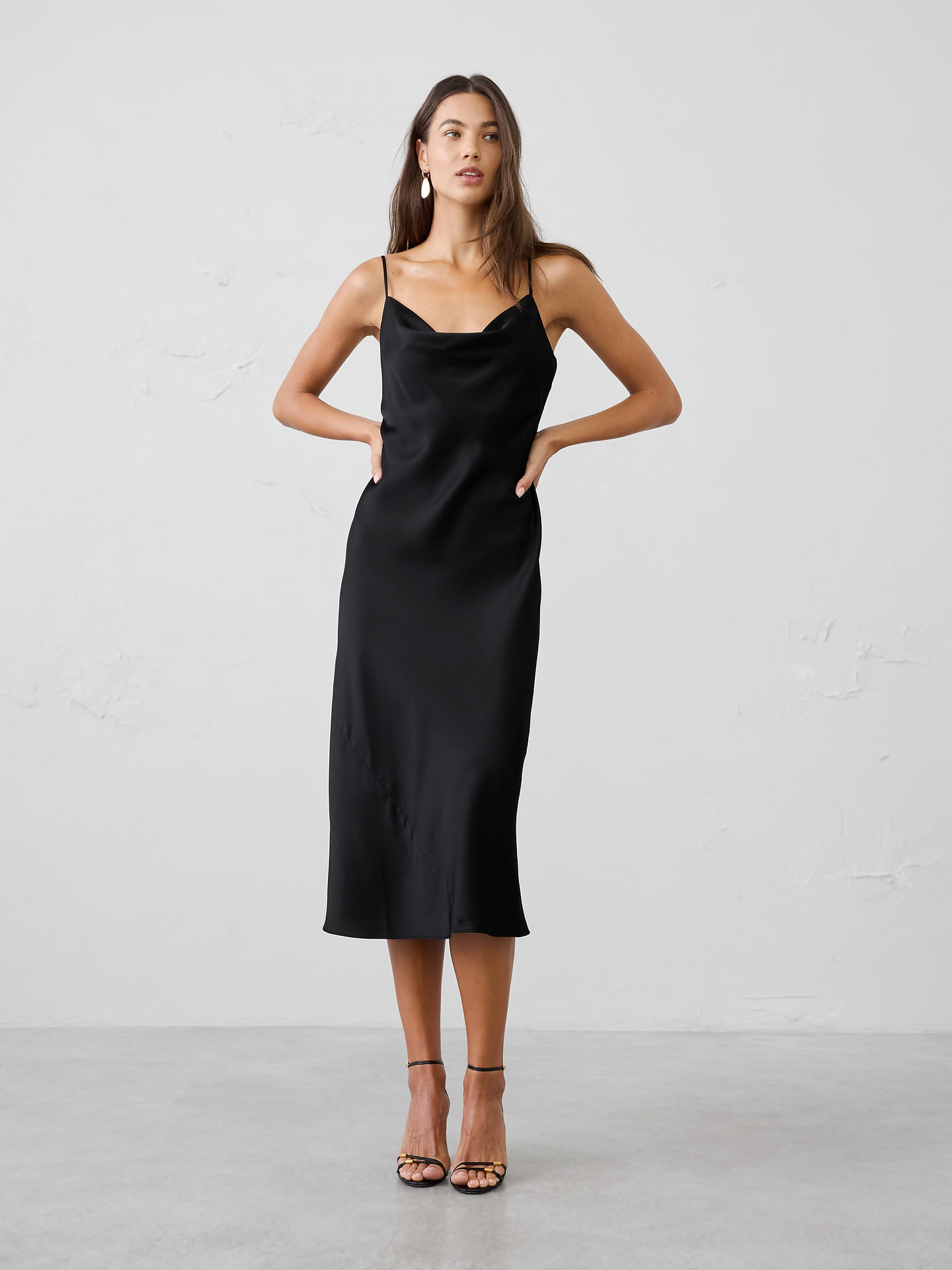 Image 1 of 4, Our best‑selling satin slip dress is a timeless wardrobe essential, designed with a fluid silhouette and effortless drape. Elegant yet versatile, it’s the perfect piece for occasion dressing, easily styled up for special events or down for a more relaxed, polished look., Soft cowl neckline. Adjustable spaghetti straps., Bias‑cut satin fabrication enhances fluid drape and movement., Fitted at the waist., Flared hem creates a soft, flowing silhouette., Made exclusively for Banana Republic Factory., Product #1185680