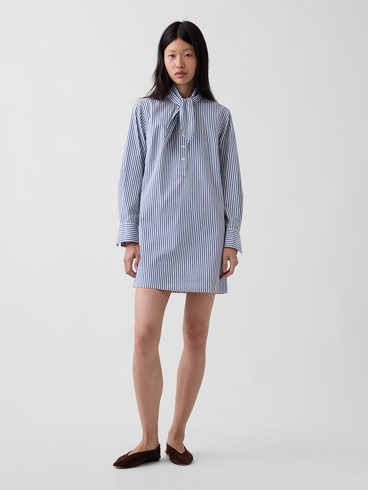 Image 1 of 5, Smooth cotton poplin mini shift dress., Tie neck with front button placket., Long sleeves with button cuffs., Back yoke seam., Made with 100% organically grown cotton which is grown without the use of synthetic pesticides and fertilizers., This product was made in a factory that invests in gender equity and women’s empowerment through RISE. Learn more at gapinc.com/equity ., Product #1184719