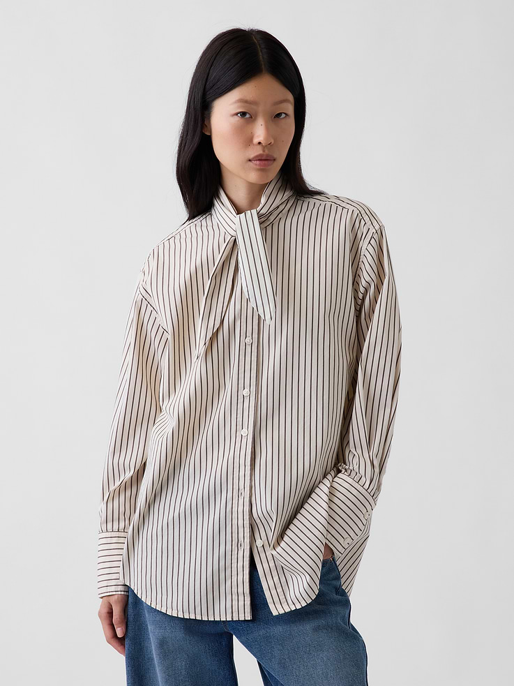 Image 1 of 5, Our oversized shirt pulled straight from the archives. Always easy. Forever iconic., Organic cotton poplin button-up shirt. In an oversized fit and longer length., Tie neck, button front., Long sleeves with button cuffs., Back yoke seam., Shirttail hem., Made with 100% organically grown cotton which is grown without the use of synthetic pesticides and fertilizers., This product was made in a factory that invests in gender equity and women’s empowerment through RISE. Learn more at gapinc.com/equity ., Product #1184843
