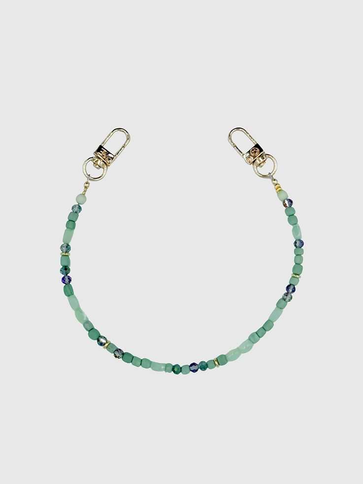 Image 1 of 1, Clover is a sophisticated accessory designed to complement your style with subtle beauty and practicality., This wristlet is handcrafted with a delicate arrangement of soft green beads, and hints of gold, creating a serene and harmonious look., With its minimalist design, Clover is perfect for those who appreciate minimalistic design., Universal Phone Hitch required to attach to your phone case, sold separately., Over time, certain bead colors may lose their vibrancy due to exposure to air, water, and heat, which can result in fading, tarnishing, or rubbing off., Due to natural variations in gemstones and beads, product may differ slightly from displayed photos., THE CÆP in no way guarantees the integrity of your smartphone or screen when using this strap. Handle with care and employ your cell phone at your own risk.