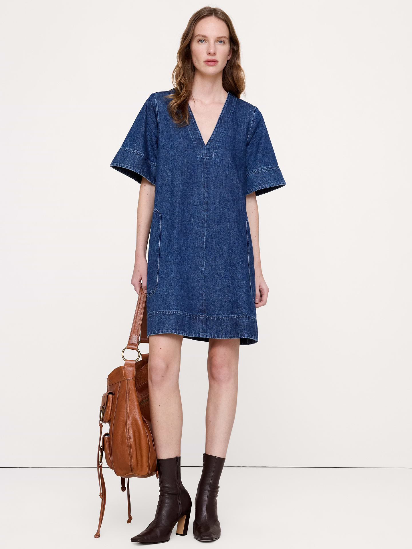 Image 1 of 6, Your new partner in crime, this denim mini dress is finished with a garment wash for already-loved softness and lived-in color., Trapeze Fit: Straight through the bust and waist, A-line skirt., V-neck., Side seam pockets., Unlined., Product #873257