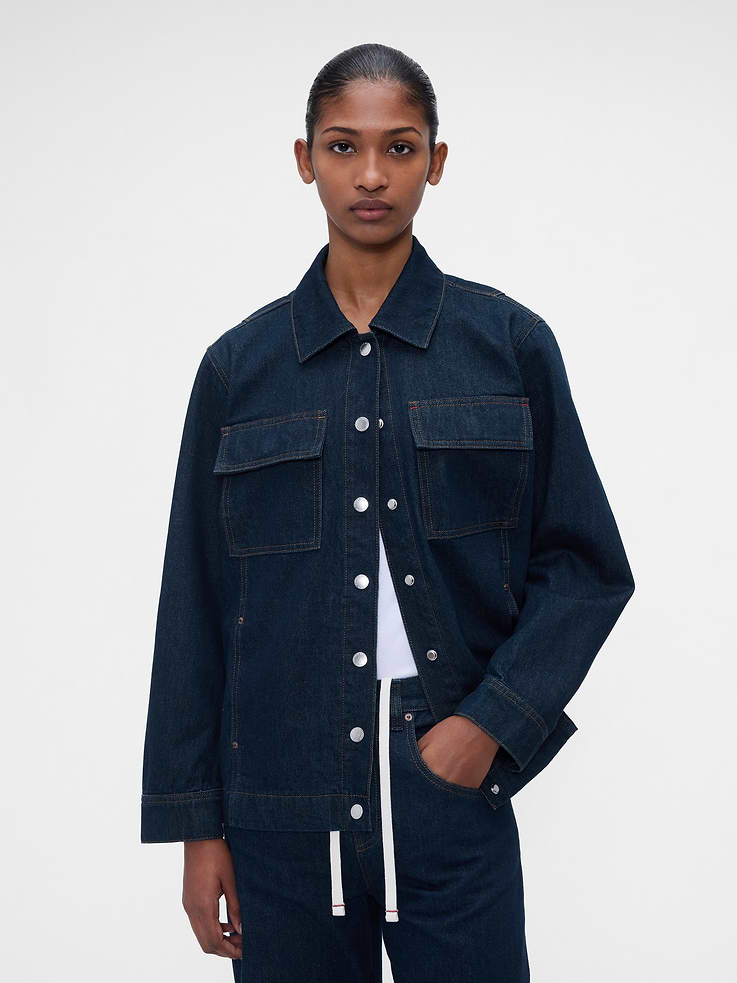 Image 1 of 9, Rigid denim shirt jacket. In a relaxed fit., Spread collar., Long sleeves with button cuffs., Logo snap button front., Flap patch pockets at chest., On-seam pockets., Gap x Victoria Beckham logo patch at rear hem., More Sustainable Cotton: Made with 5% recycled cotton. Compared to virgin materials, using recycled materials helps reduce resource use and waste., Responsibly Made: This shirt jacket is part of our water-saving Washwell program. Compared with conventional wash methods, Washwell uses at least 20% less water., Product #1185491