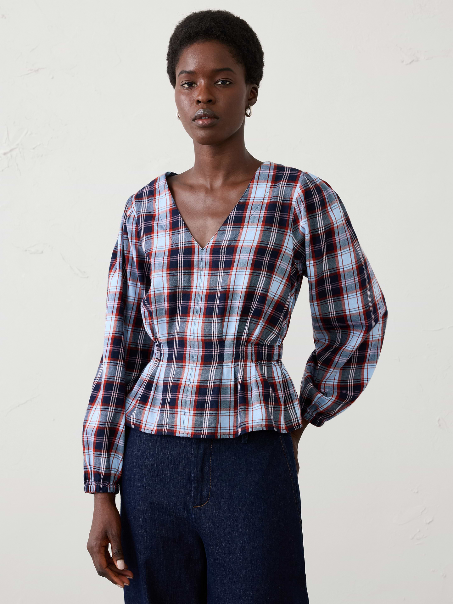 Image 1 of 4, Feminine details meet cozy comfort in this flannel blouse, designed to elevate holiday casual dressing. Crafted from a soft plaid flannel, this style features a flattering V-neckline, voluminous sleeves, and delicate pleated detailing that creates beautiful shape and texture through the bodice., V-neckline. Voluminous long sleeves with elasticized cuffs., Delicate pleated detailing., Back smocking at waist., Peplum hem., Made exclusively for Banana Republic Factory., Product #1185901