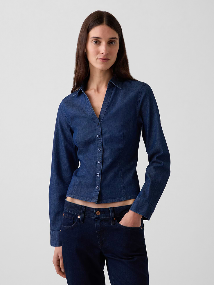 Image 1 of 5, Low-stretch denim fitted button-up shirt. In a slightly cropped length., Spread collar, v-neck., Long sleeves with button cuffs., Button front., Princess darts at front and back., Dark indigo wash., Responsibly Made: This denim shirt is part of our water-saving Washwell program. Compared with conventional wash methods, Washwell uses at least 20% less water., More Sustainable Materials: Made with 15% recycled polyester and 5% recycled cotton. Compared to virgin materials, using recycled materials helps reduce resource use and waste., This product was made in a factory that invests in gender equity and women’s empowerment through RISE. Learn more at gapinc.com/equity ., Product #1184823
