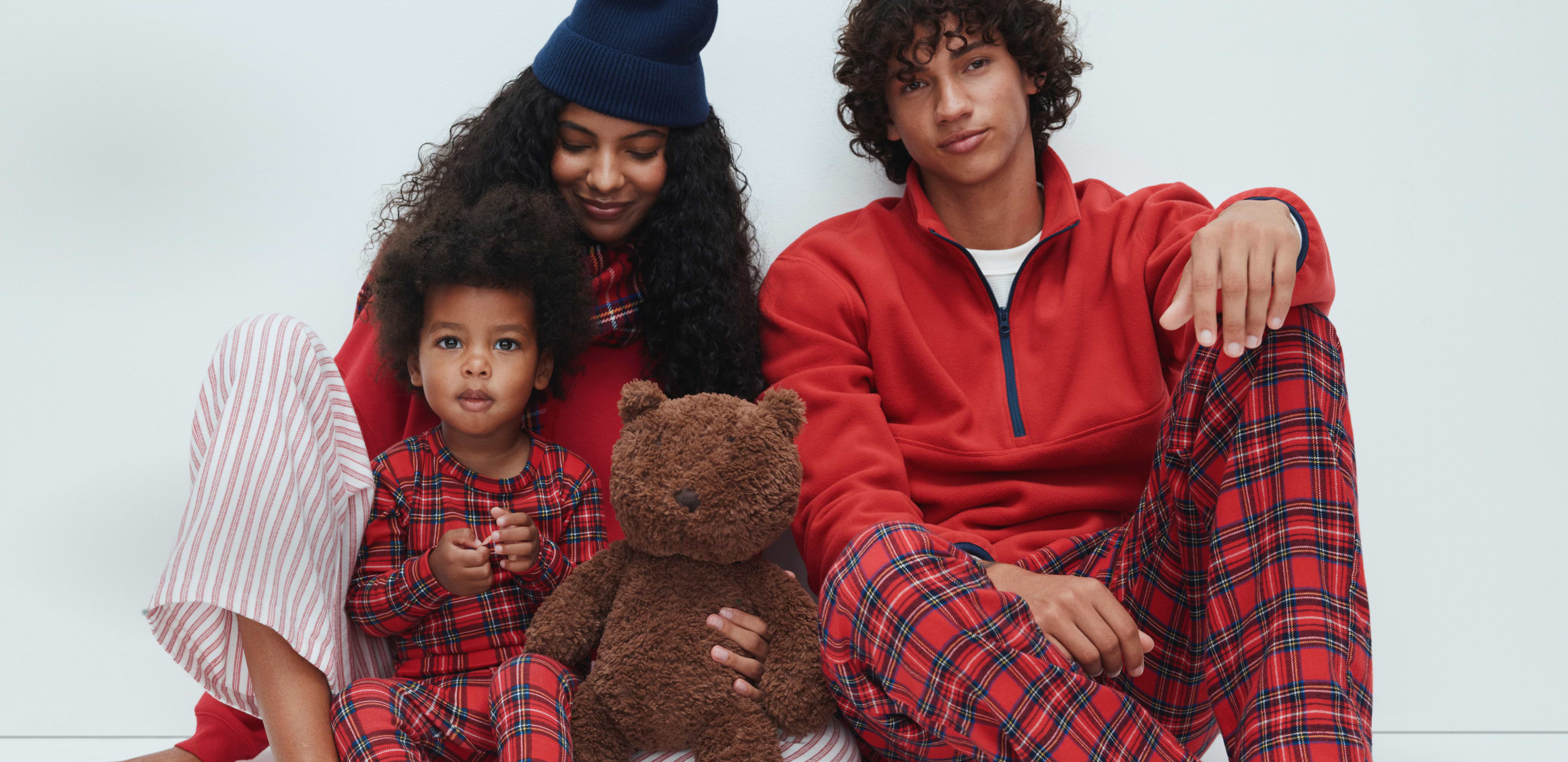 Three people in red and plaid pajamas sit together; a child holds a brown teddy bear.