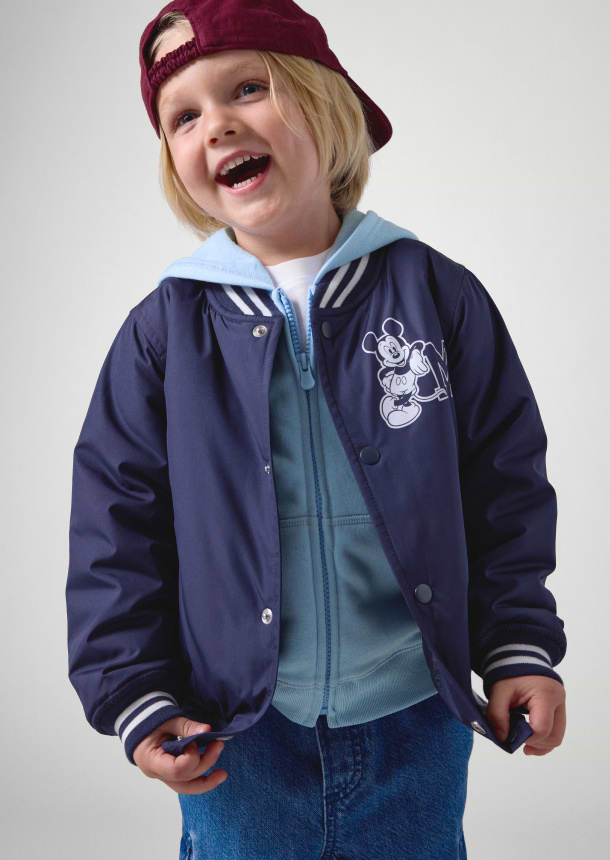 a young boy in a mickey mouse jacket and hat smiling