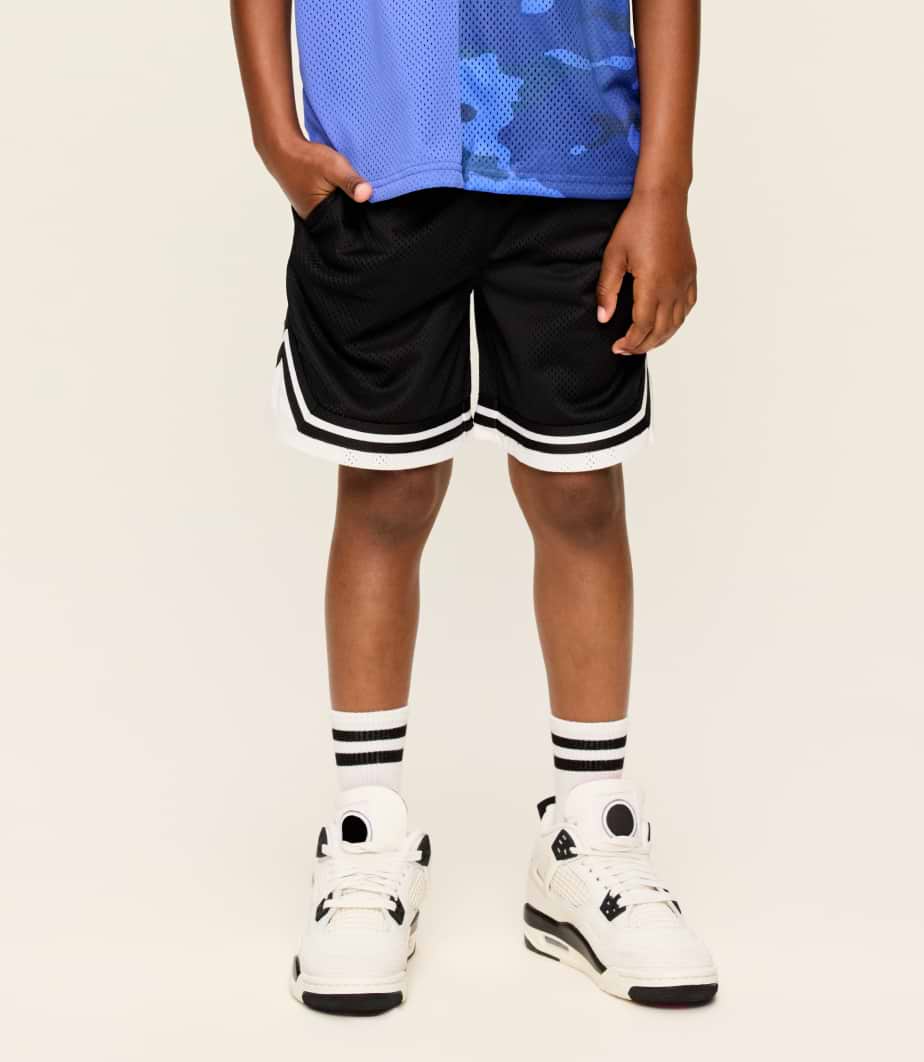 Child wearing black mesh basketball shorts with white trim, white socks with black stripes, and white high-top sneakers, standing against a plain background.