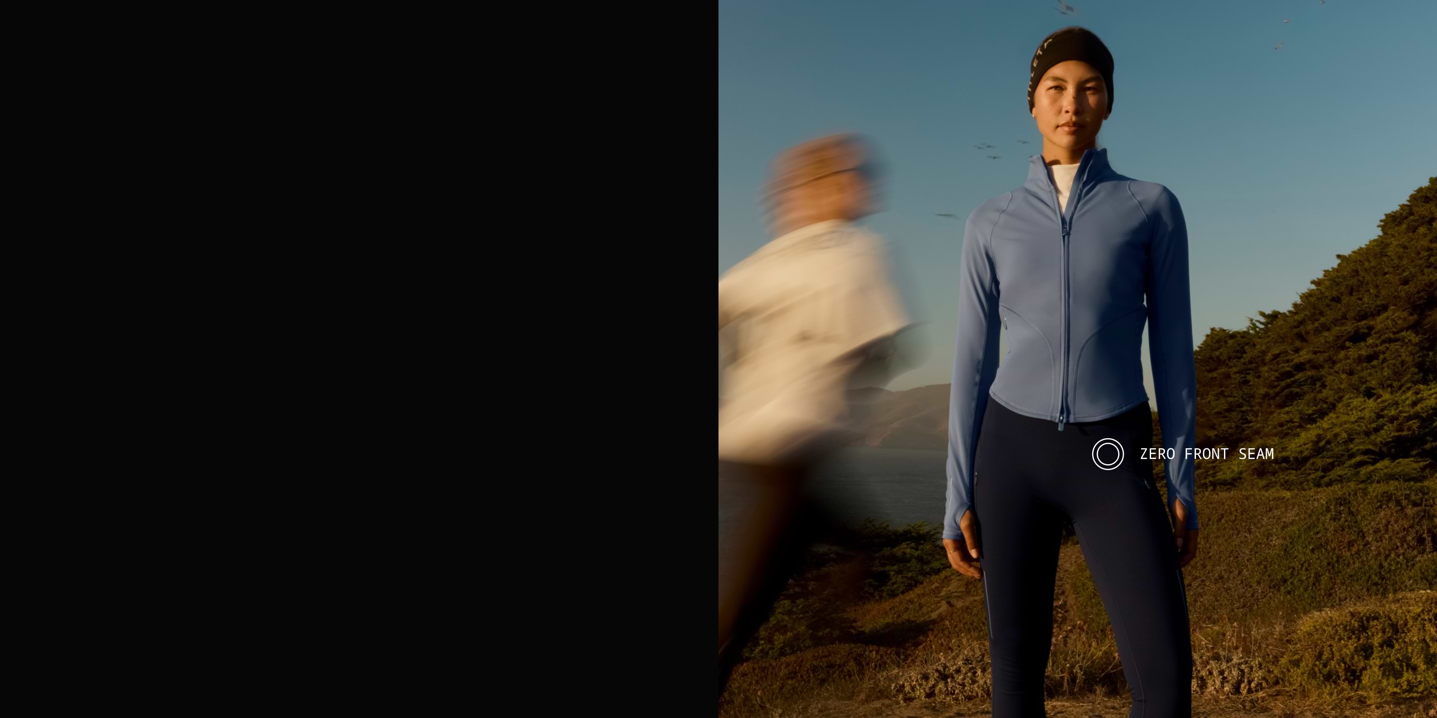 Person in a blue zip jacket and dark leggings stands on a coastal trail at dusk while a blurred runner passes; label highlights “Zero Front Seam.”