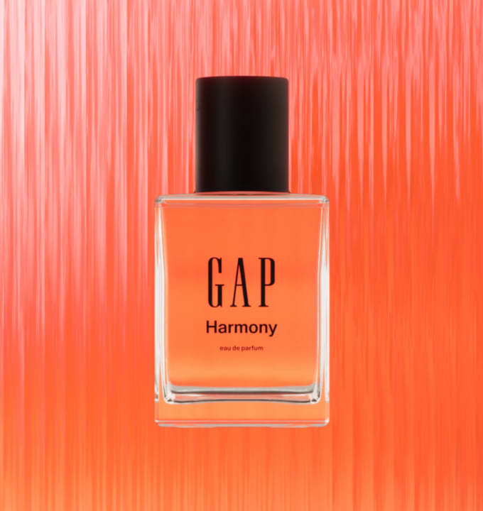 Square glass perfume bottle labeled “GAP Harmony” with a black cap, orange liquid, on a textured orange background.