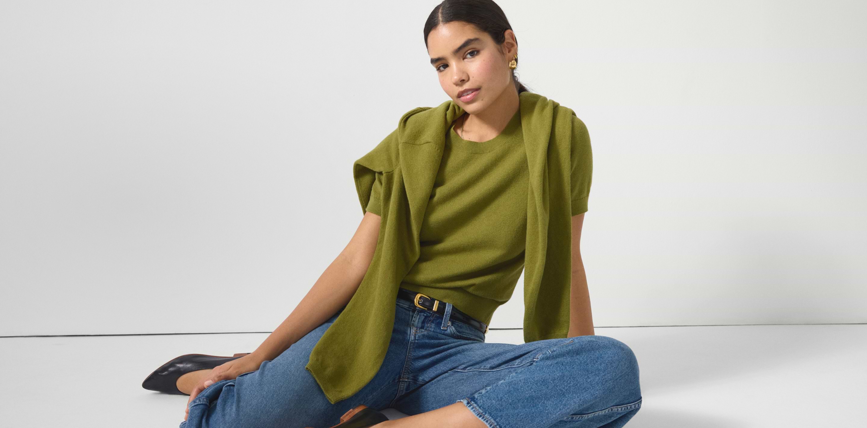 a woman sitting on the floor wearing a green shirt and jeans