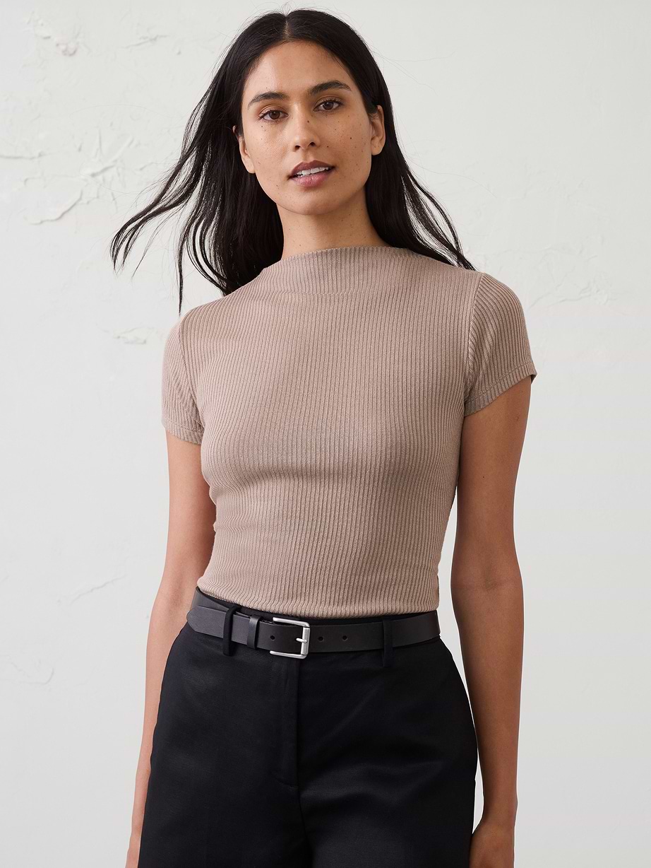 Person in a ribbed beige short-sleeve top and black belted pants against a plain background.