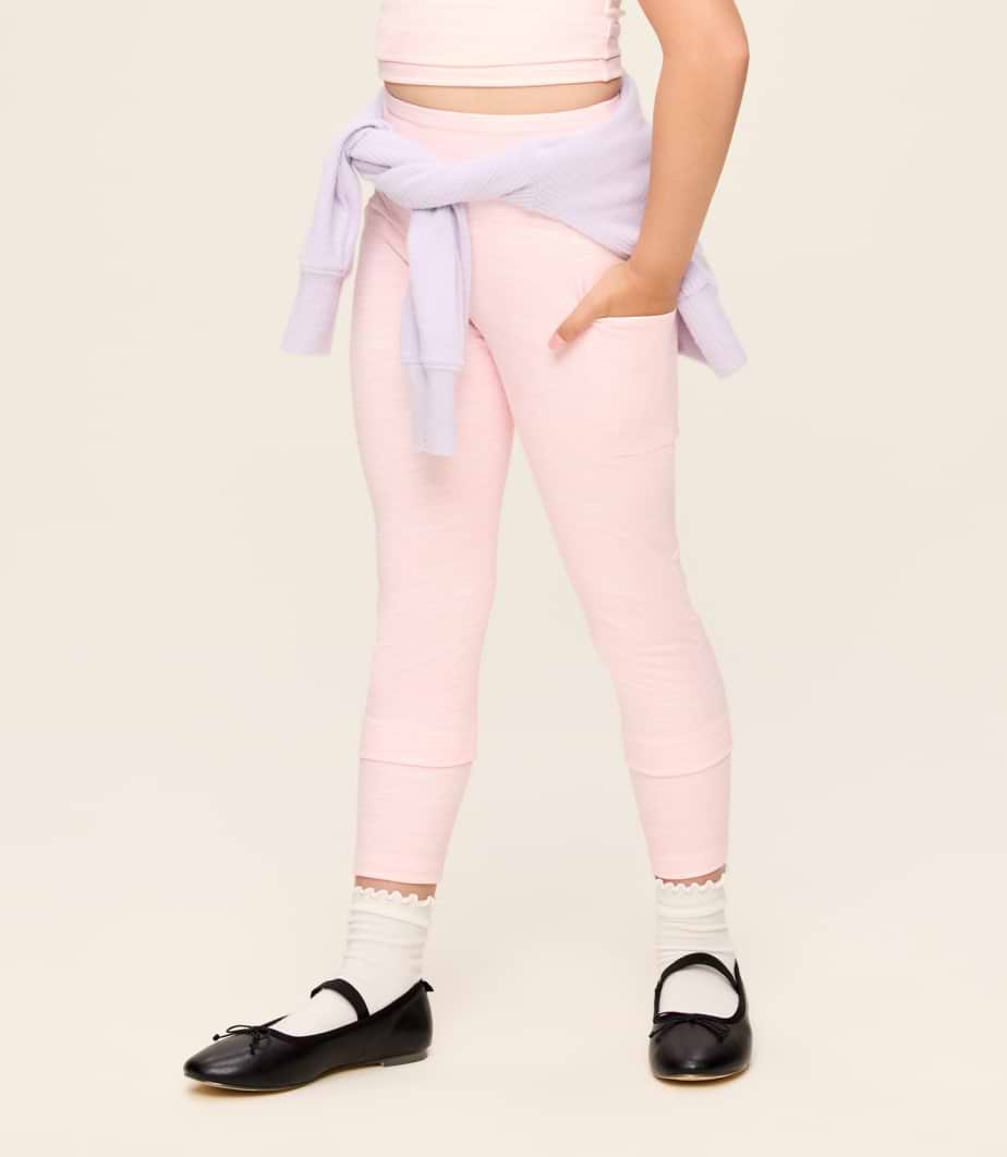Child in pink leggings with pockets, lavender sweater tied at the waist, white socks, and black Mary Jane flats.
