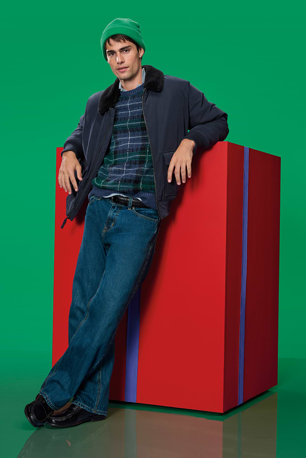 A male model dressed in plaid sweater, dark jacket and straight jeans.