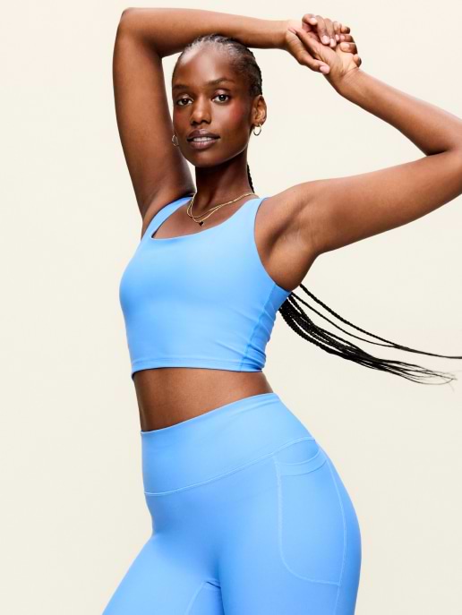Person posing with arms raised, wearing a light blue sports bra and leggings.