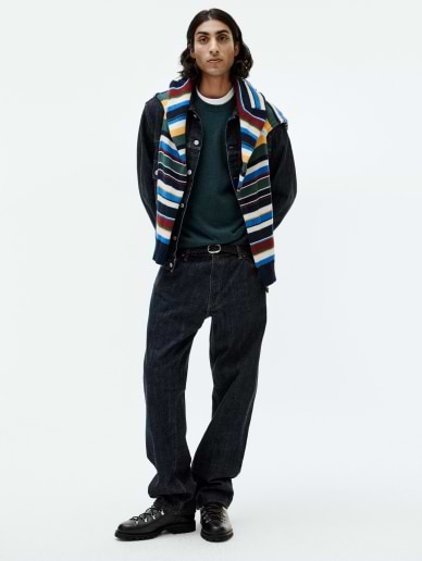 a man in a striped vest and jeans poses for a photo