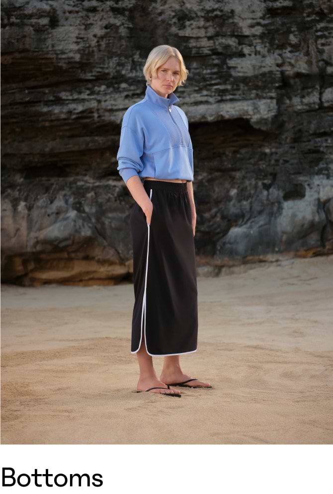 Person in a black midi skirt with white piping and side slit on a sandy beach; caption reads “Bottoms.”