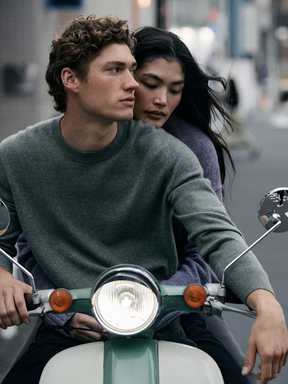 Two people on a scooter, passenger hugging the driver on a city street.