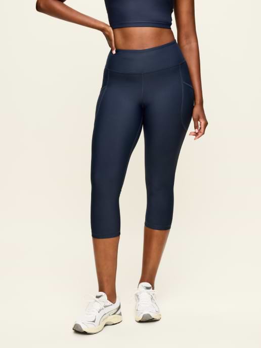 Model wearing high‑waisted navy capri leggings with side pockets and white sneakers against a plain light background.