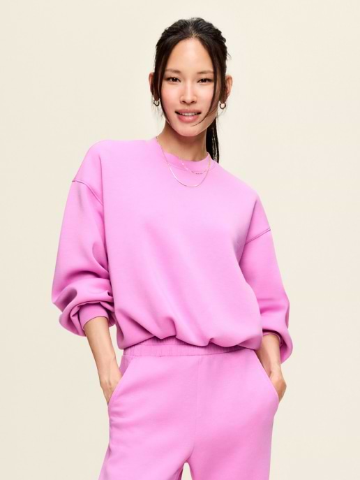 Person wearing a bright pink sweatshirt and matching joggers, smiling with hands in pockets against a plain background.