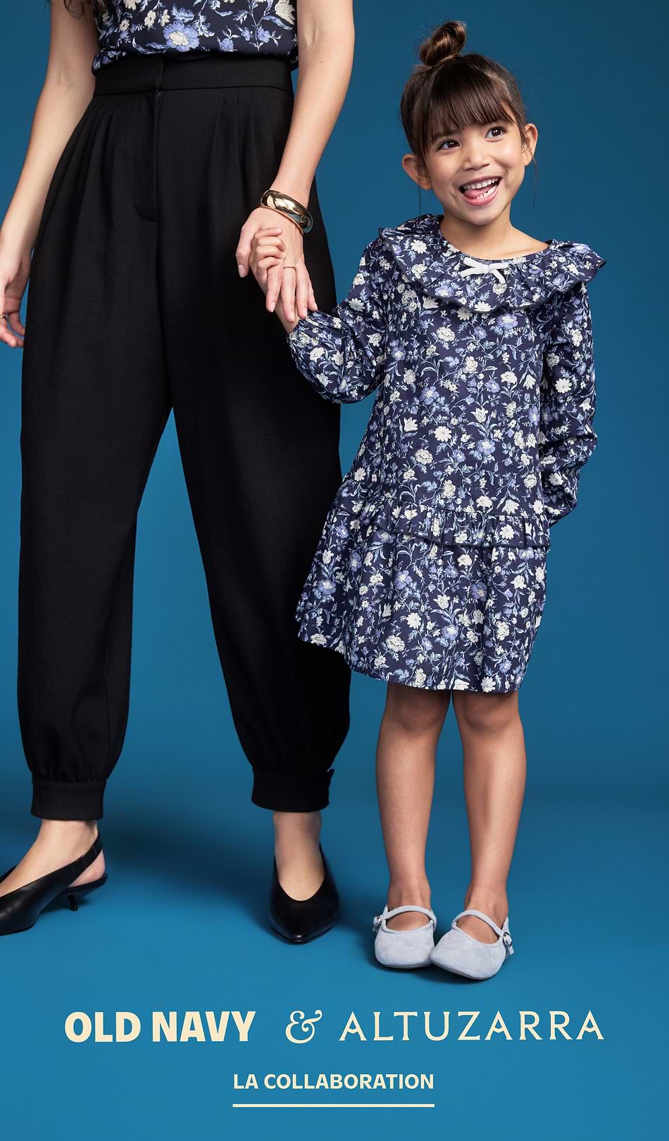Alt text: Smiling girl in a blue floral dress holds an adult’s hand against a blue backdrop; Old Navy x Altuzarra ad.