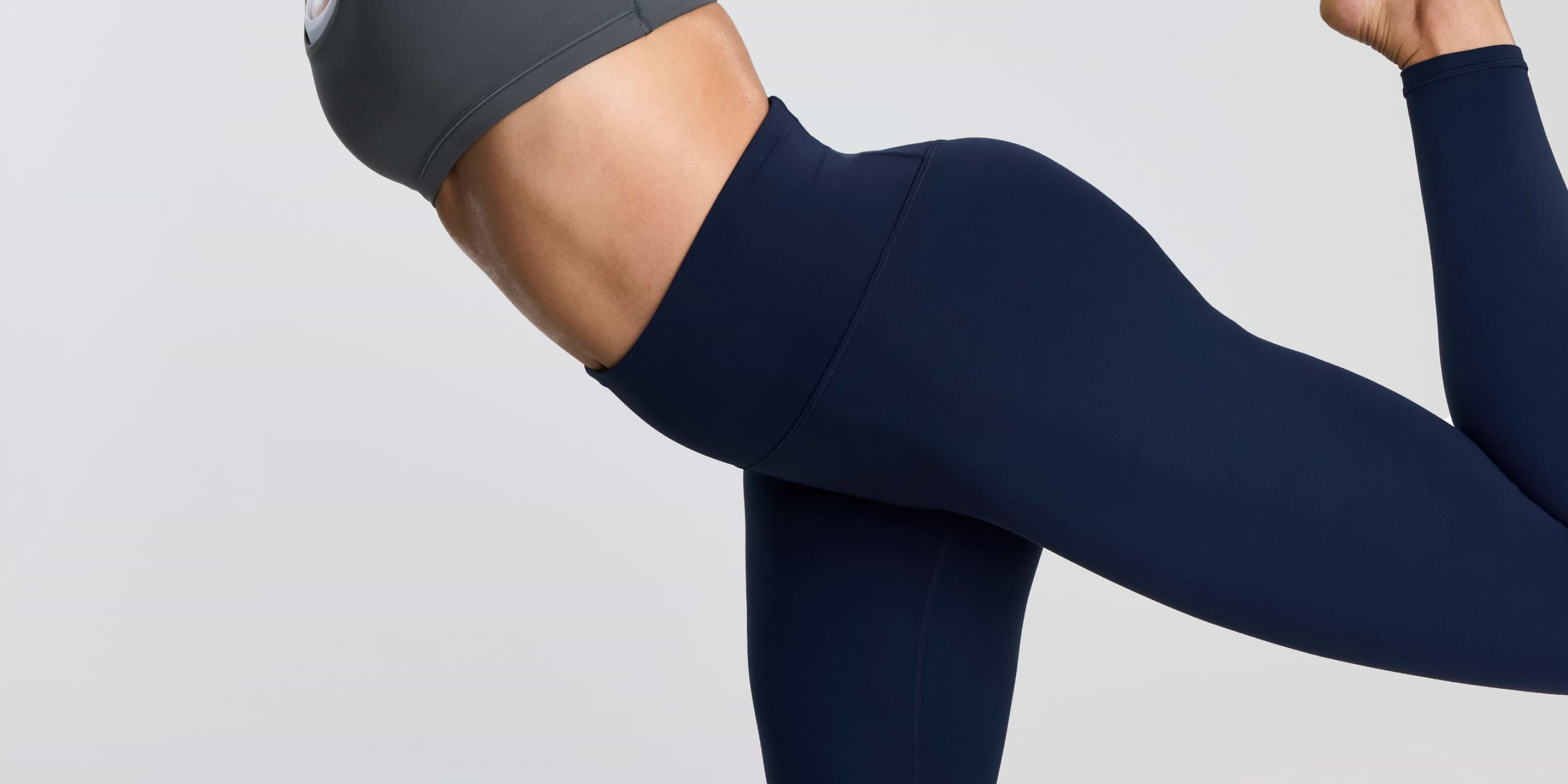 Close-up side view of a person in navy leggings and a gray top holding a lunge pose.