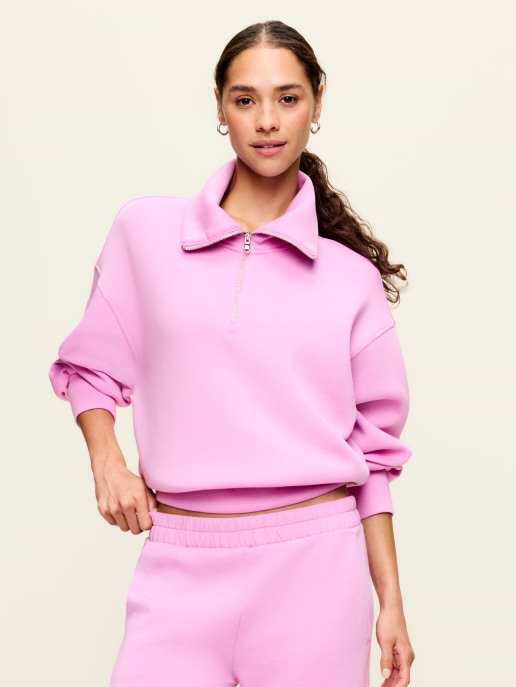 Person wearing a pink quarter-zip sweatshirt and matching joggers, posing against a plain background.