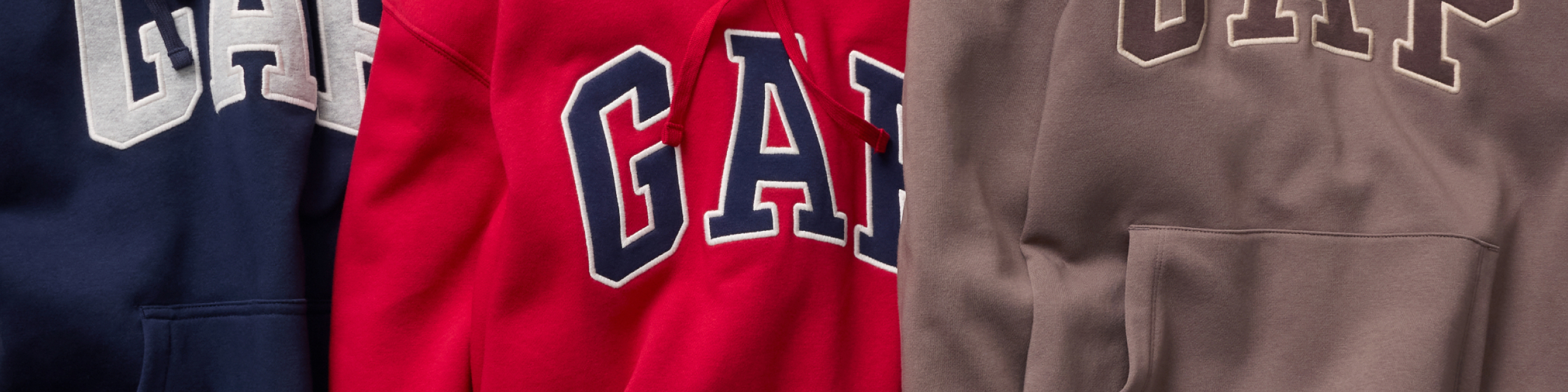 Close-up of navy, red, and taupe hoodies with large “GAP” logos.