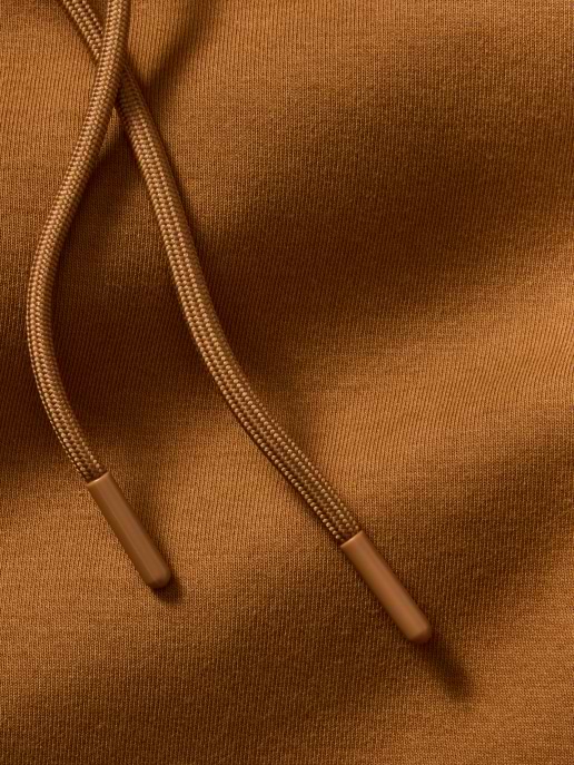 Close-up of two brown hoodie drawstrings with plastic tips on caramel-colored sweatshirt fabric.