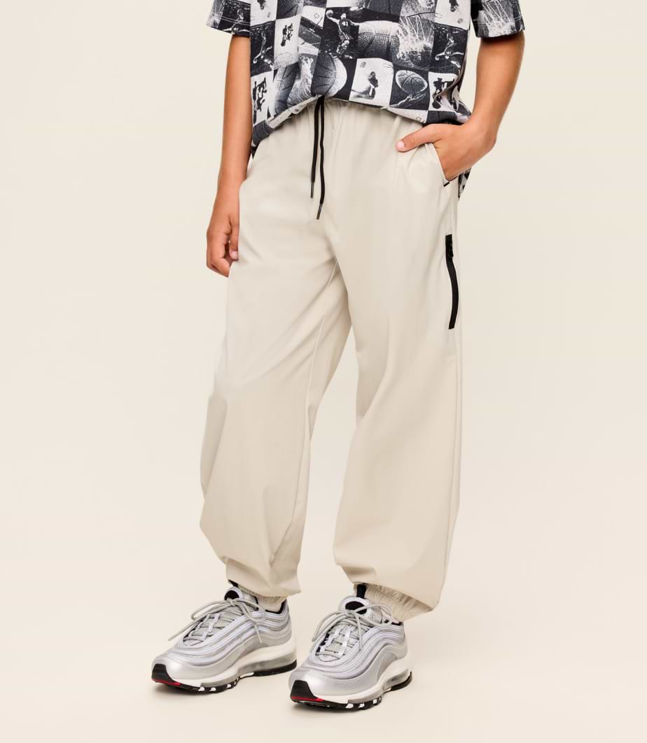 Person wearing light beige baggy drawstring pants with elastic cuffs and a side zip pocket, paired with silver sneakers.