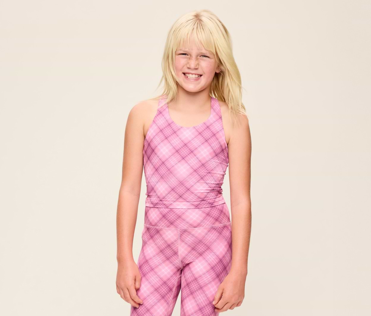 Smiling child in a pink plaid sleeveless top and matching leggings against a plain light background.