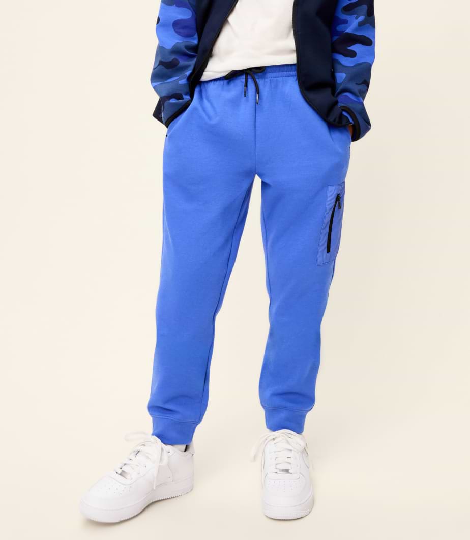Blue jogger sweatpants with drawstring waist, cuffed ankles, and a side zip pocket, worn with white sneakers.