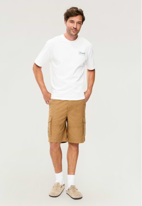 A male model wears a pair of camel colored cargo shorts.