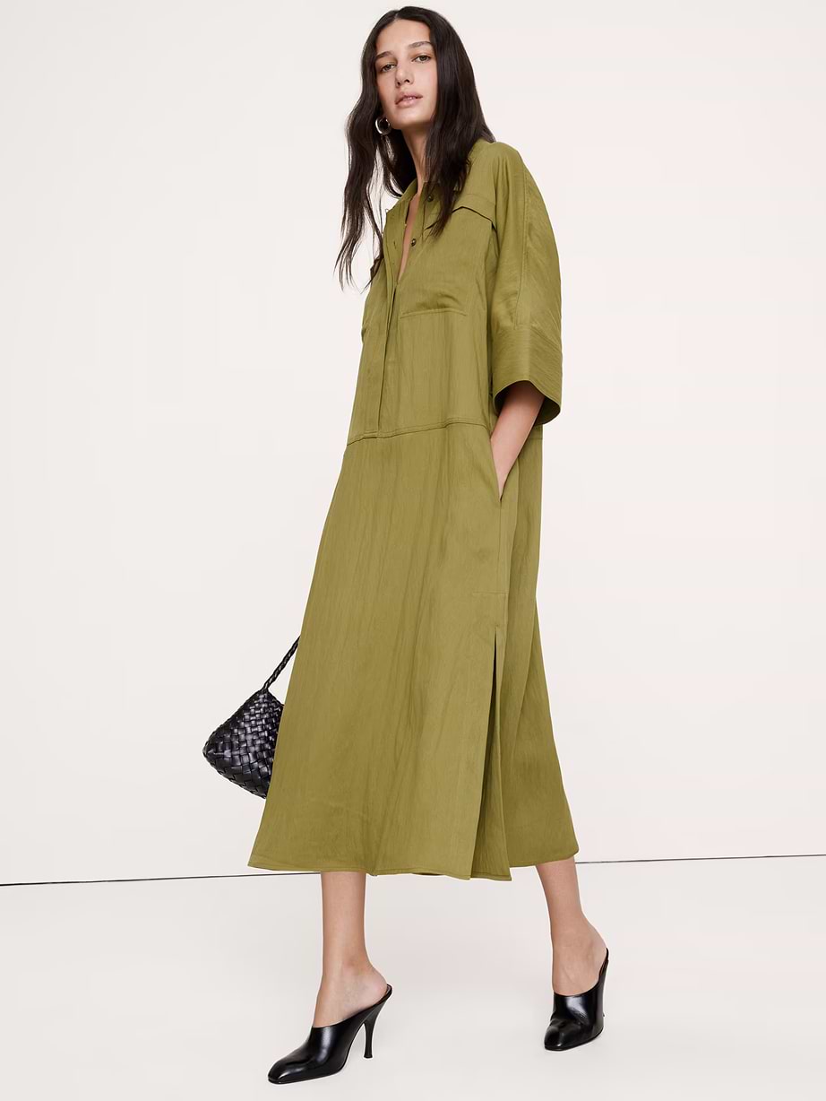 Person wearing an olive-green loose midi dress with half sleeves and side slits, black heeled mules, and a small woven black bag.