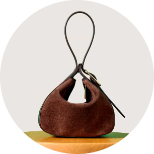 Small brown suede handbag with a looped top handle on a wooden table.