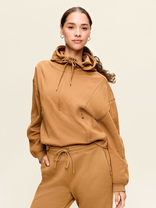 Person in tan hoodie and matching joggers against a neutral background.