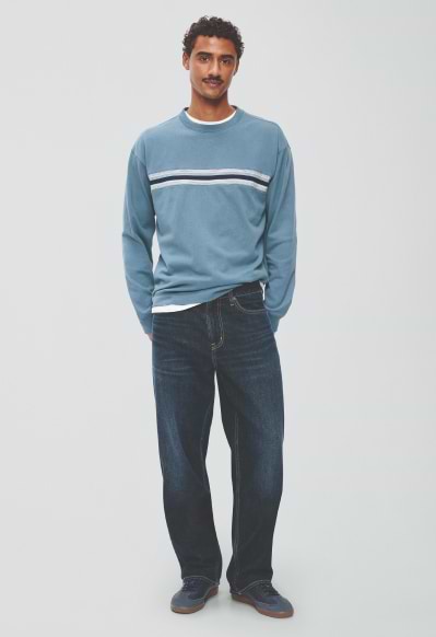 A male model wearing relaxed loose jeans and a jean jacket.