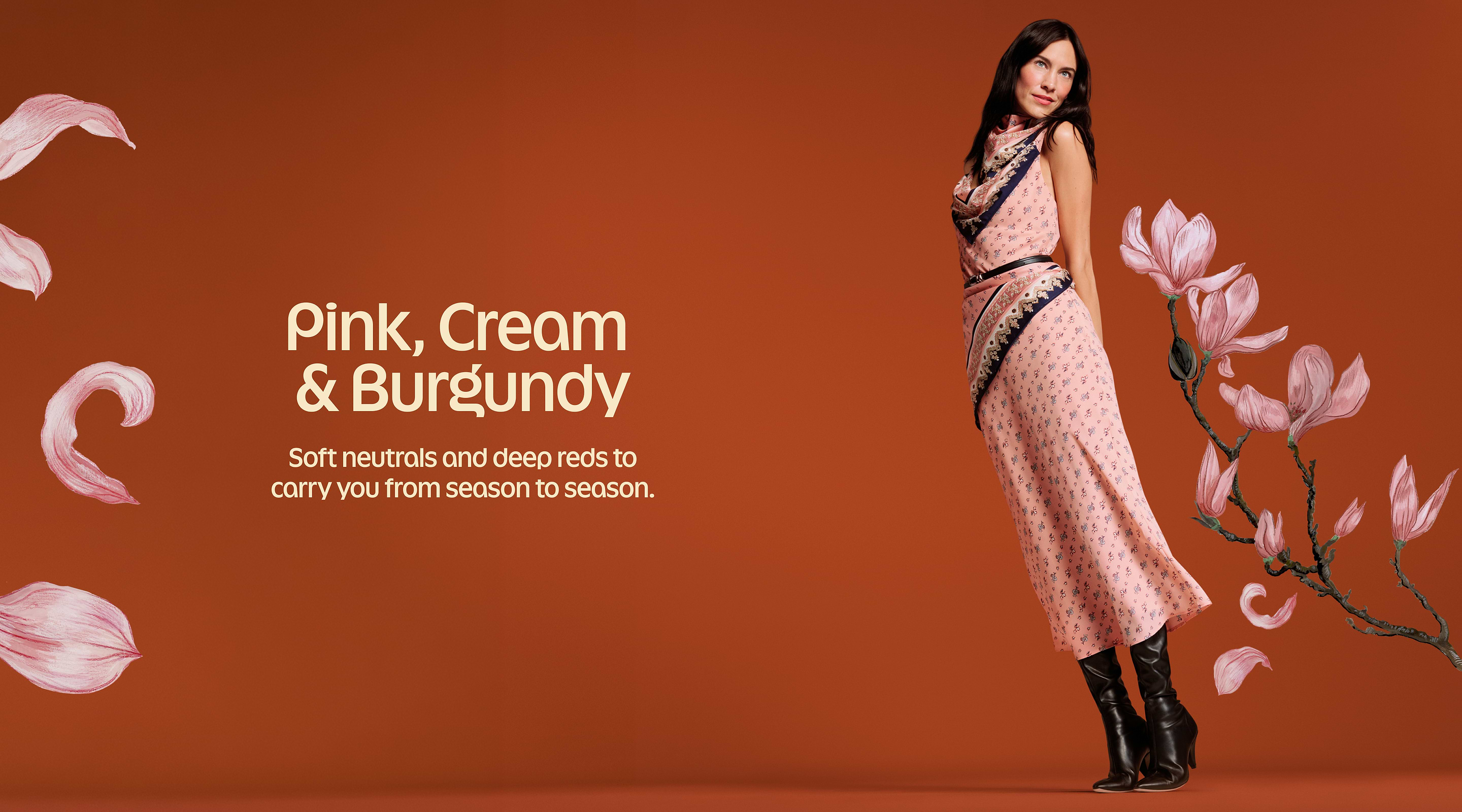 Fashion banner: a model in a pink patterned dress and black knee-high boots stands on a rust background with magnolia illustrations. Text reads “Pink, Cream & Burgundy—Soft neutrals and deep reds to carry you from season to season.”