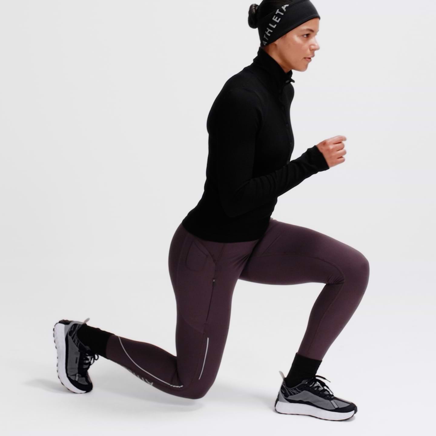 Person in athletic wear doing a forward lunge, black top and purple leggings.