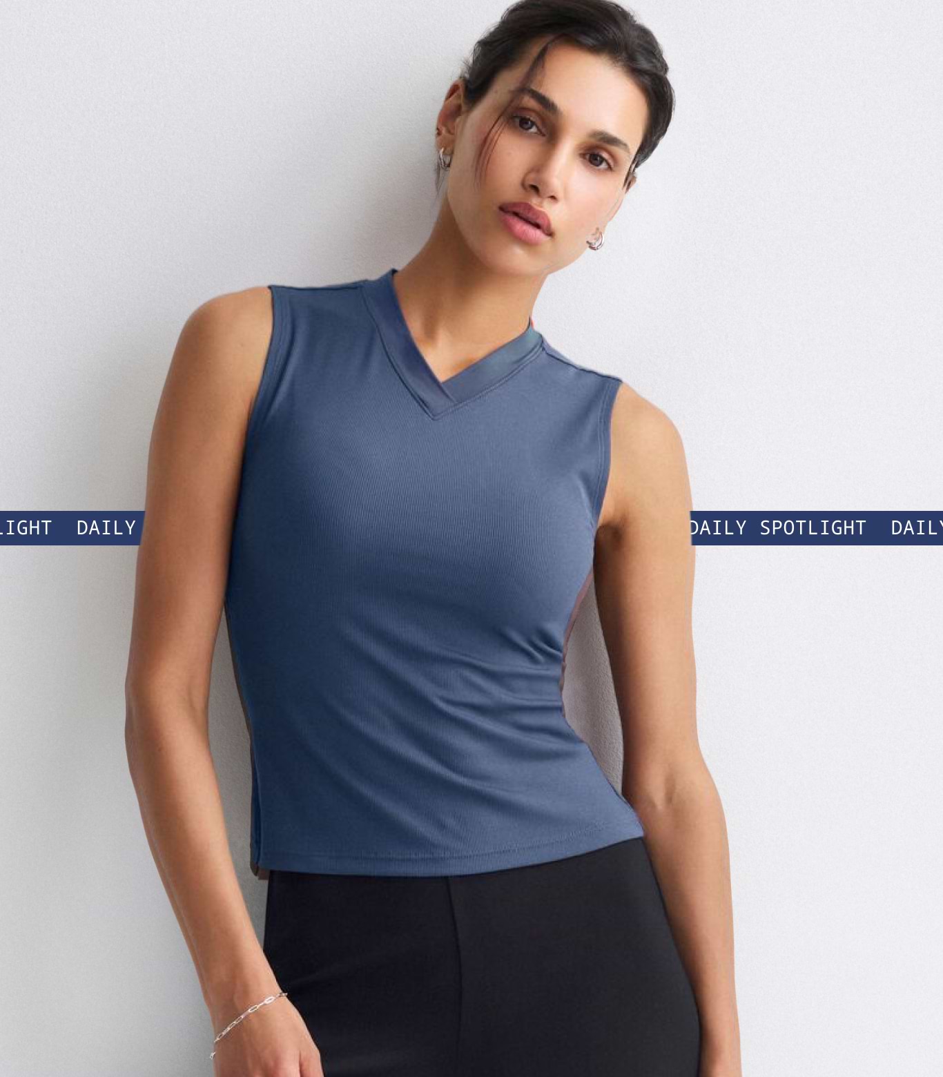 Person wearing a sleeveless blue V-neck top and black skirt against a plain wall.
