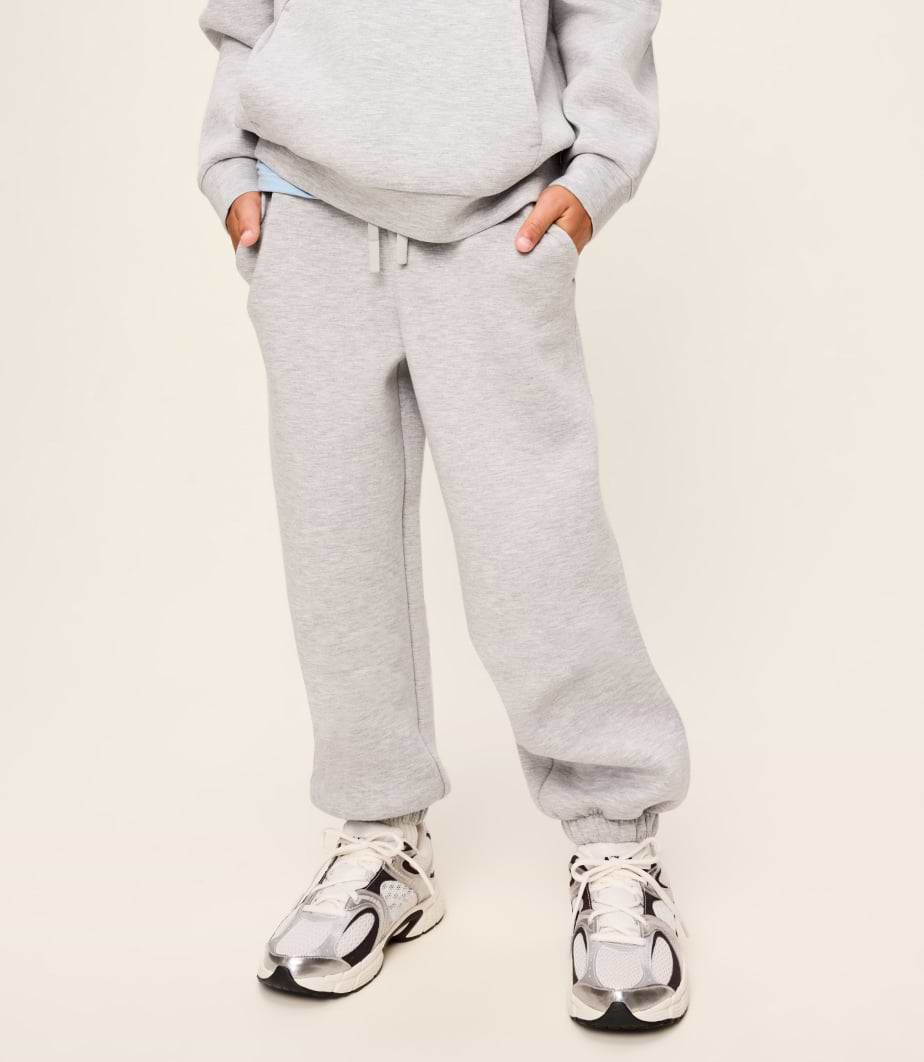 Person in light gray hoodie and sweatpants, hands in pockets, wearing chunky white sneakers.