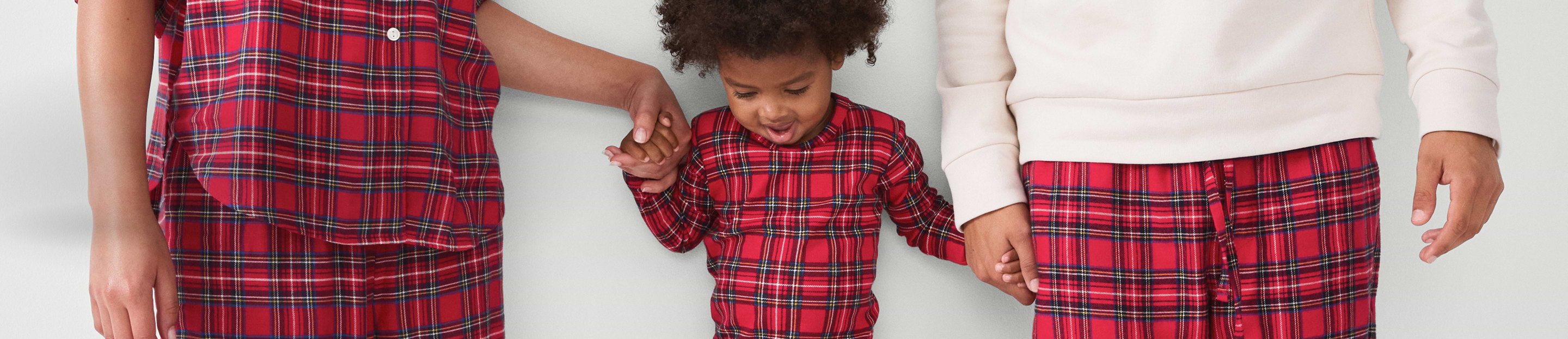 Two adults and a child in matching red plaid pajamas holding hands.