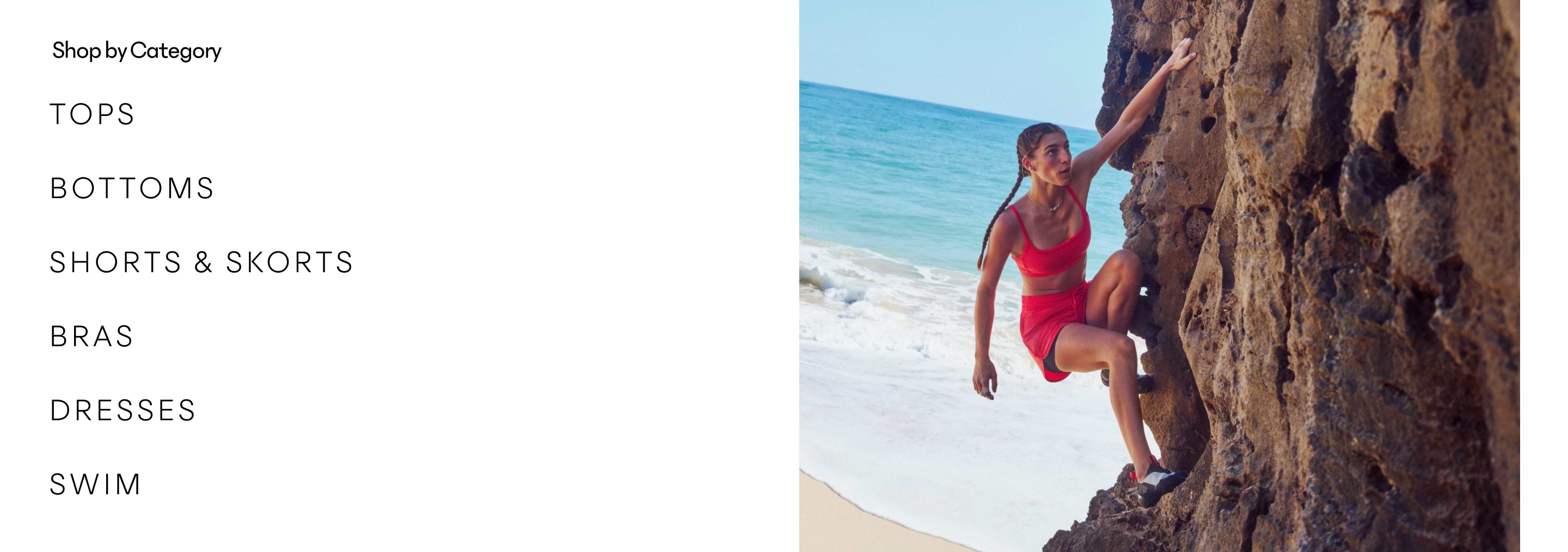 Woman in a red athletic set climbs a seaside rock wall with sandy beach and waves behind.