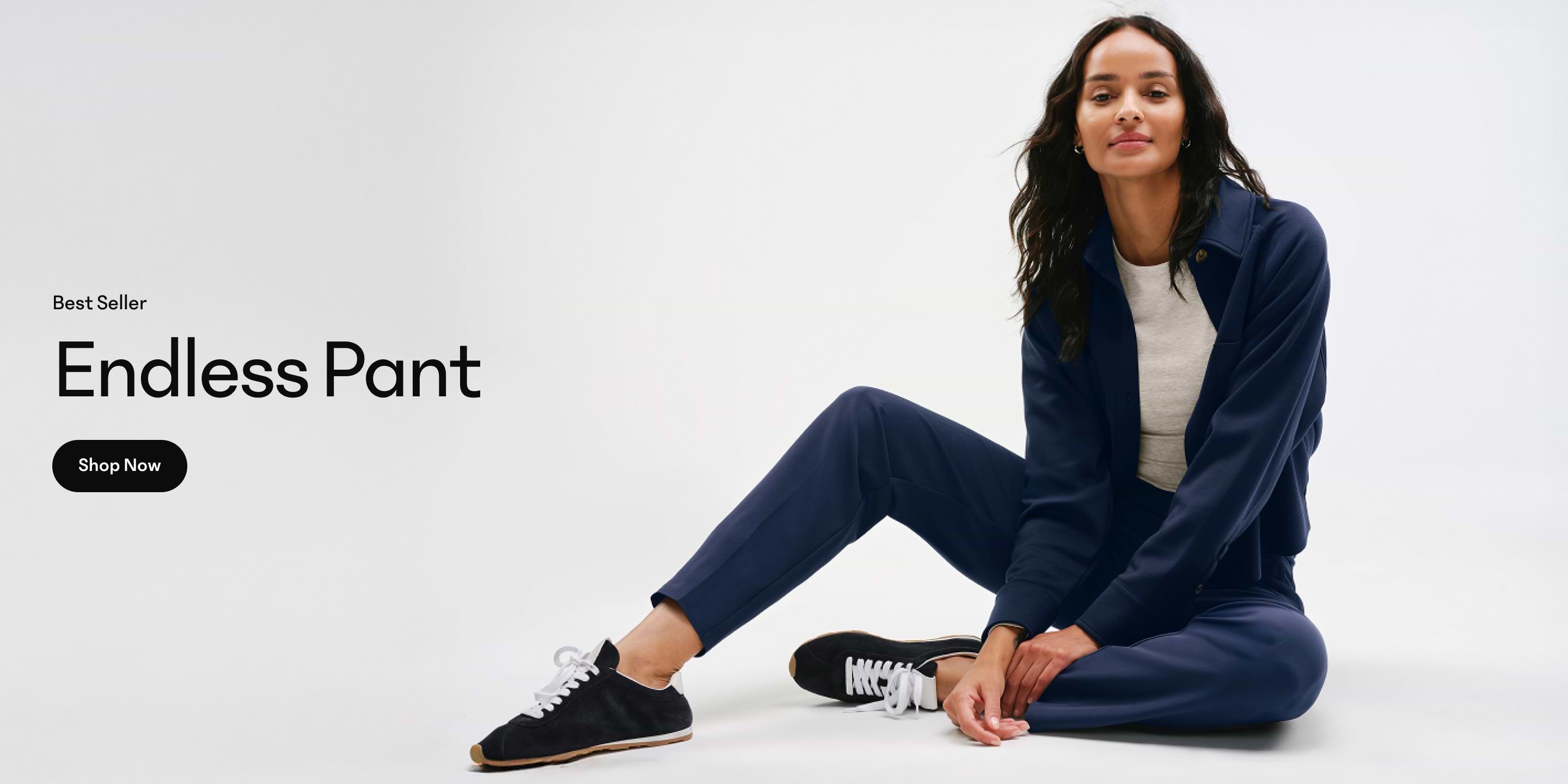 Person seated on floor wearing navy Endless Pant and matching jacket, gray top, and black sneakers on a white background; left side shows “Best Seller Endless Pant” and a Shop Now button.