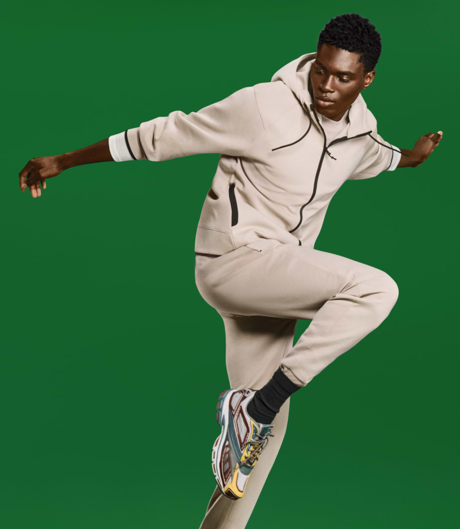 Person in burgundy athletic wear leaping mid-stride against a plain beige background.