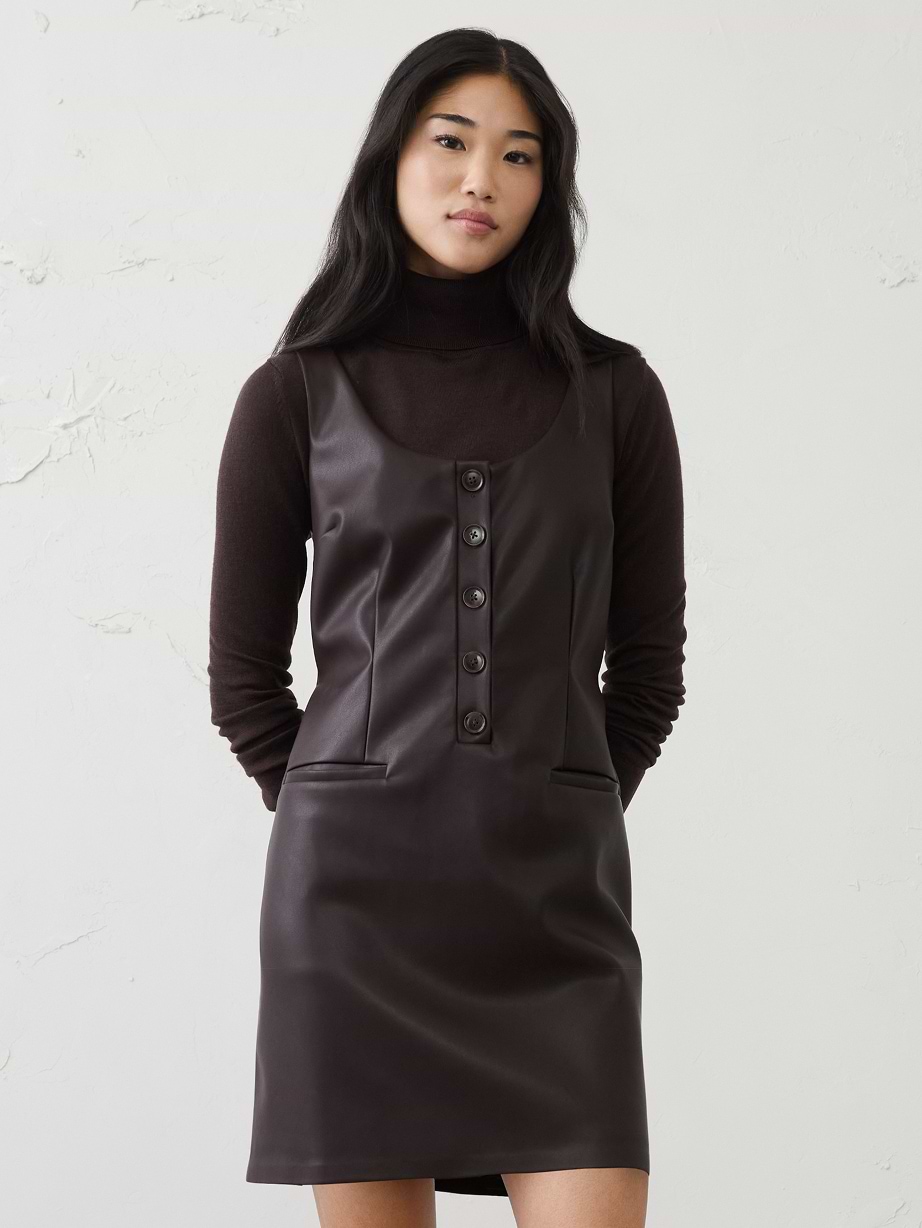 Person wearing a camel knit sweater and dark brown skirt with side buttons, standing against a plain light wall.