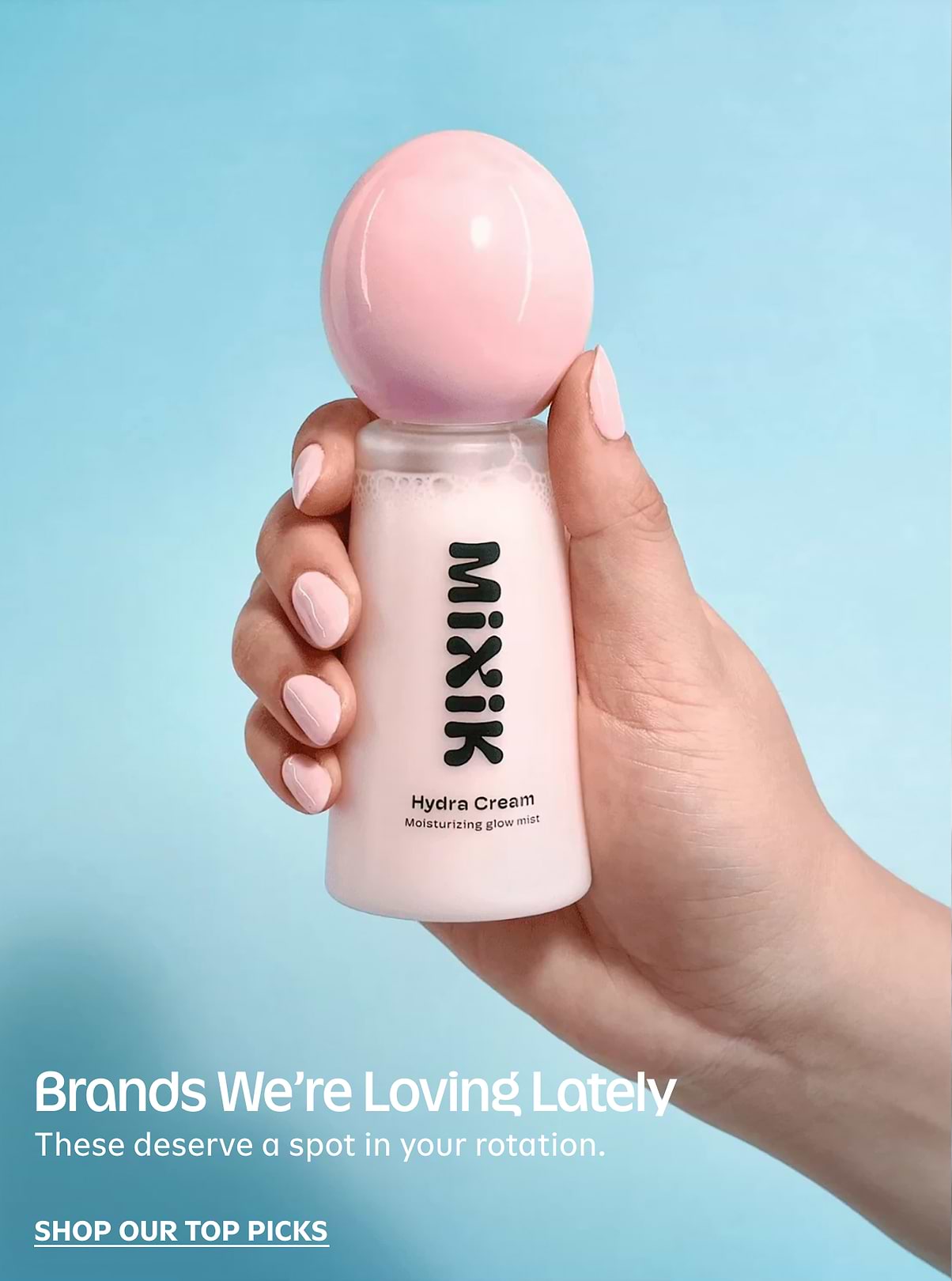 Hand holding a pink-and-white Mixik Hydra Cream bottle with a round pink cap against a blue background.