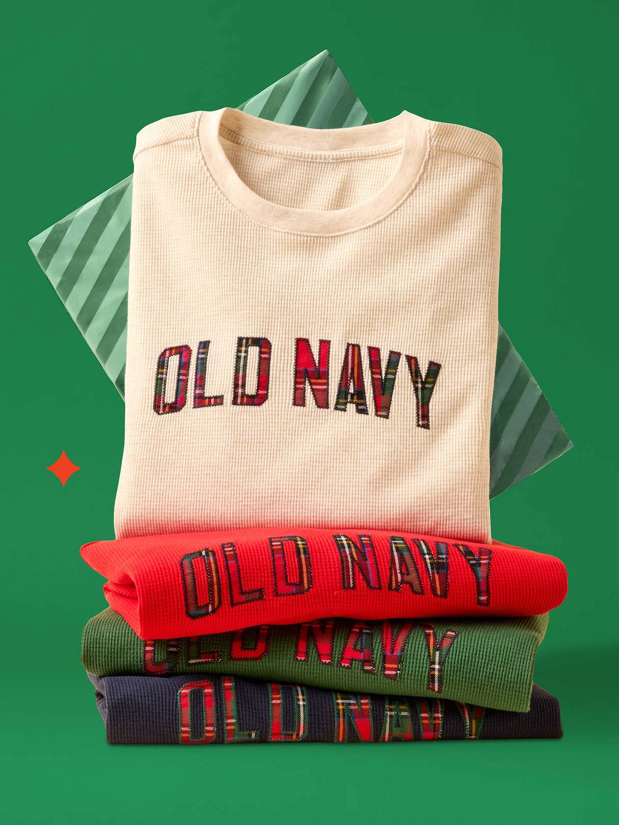 Stack of ribbed crewneck sweatshirts—cream, red, green, and navy—each embroidered with “OLD NAVY” in plaid letters, on a green background.